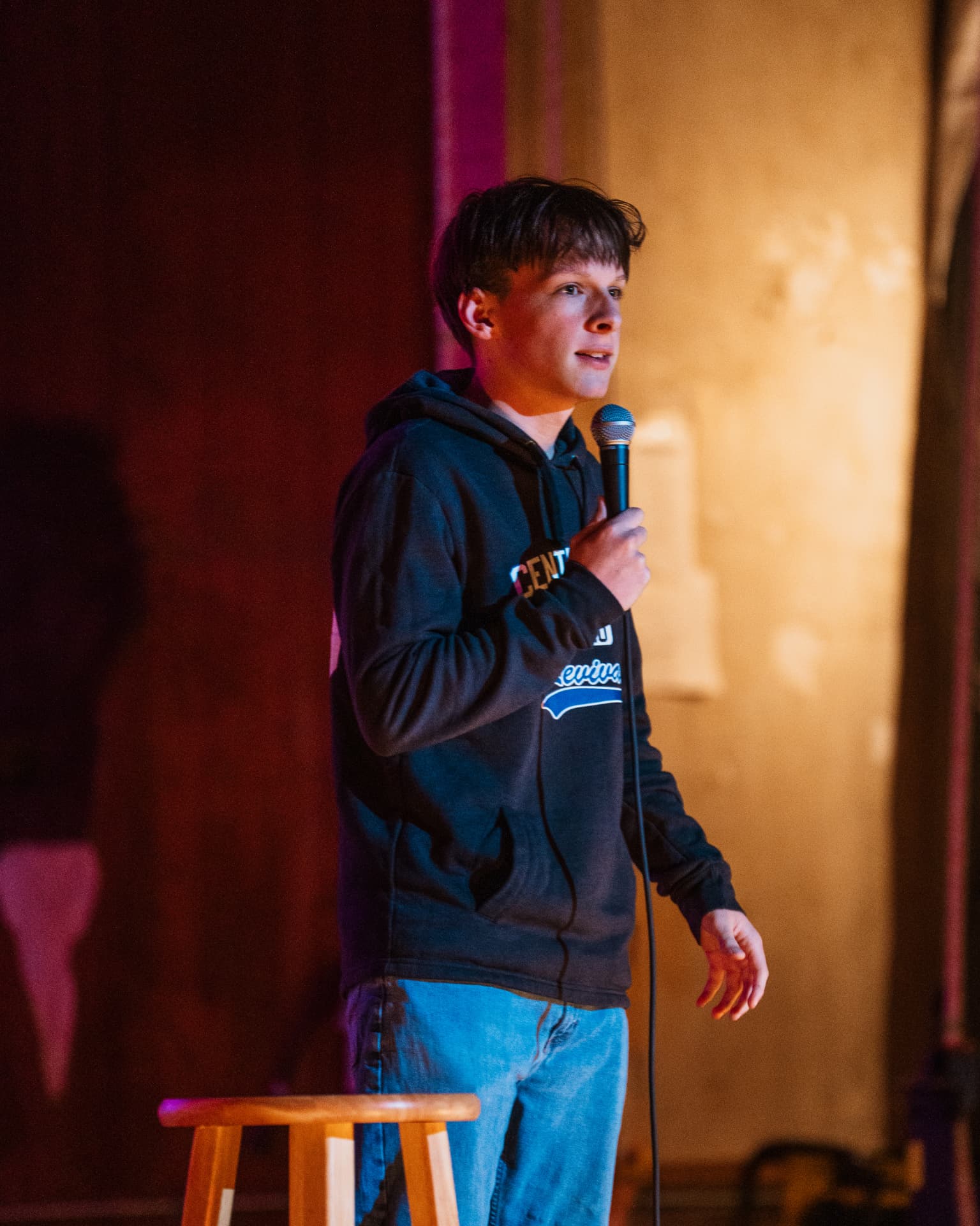 Lucas Estrella performing stand-up on stage under red and amber light