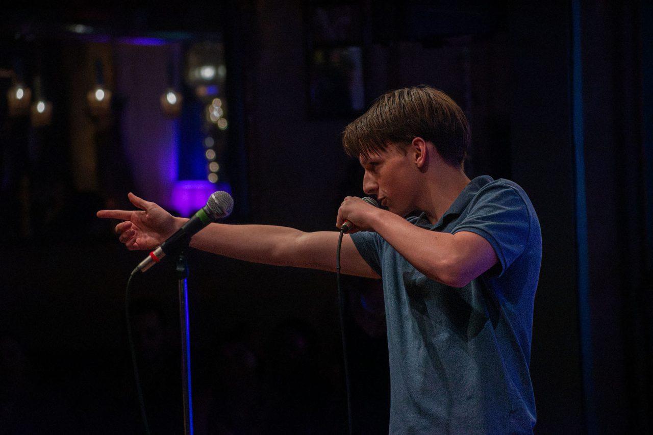 Lucas Estrella performing stand-up on stage with a microphone